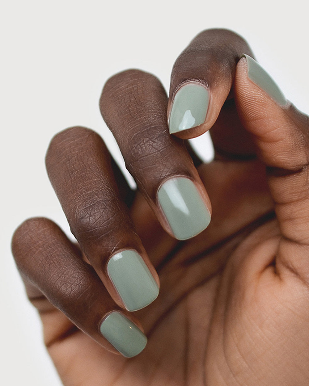 Dark skin hand wearing Soundscape sage green crème nail polish by Sienna Byron Bay close-up