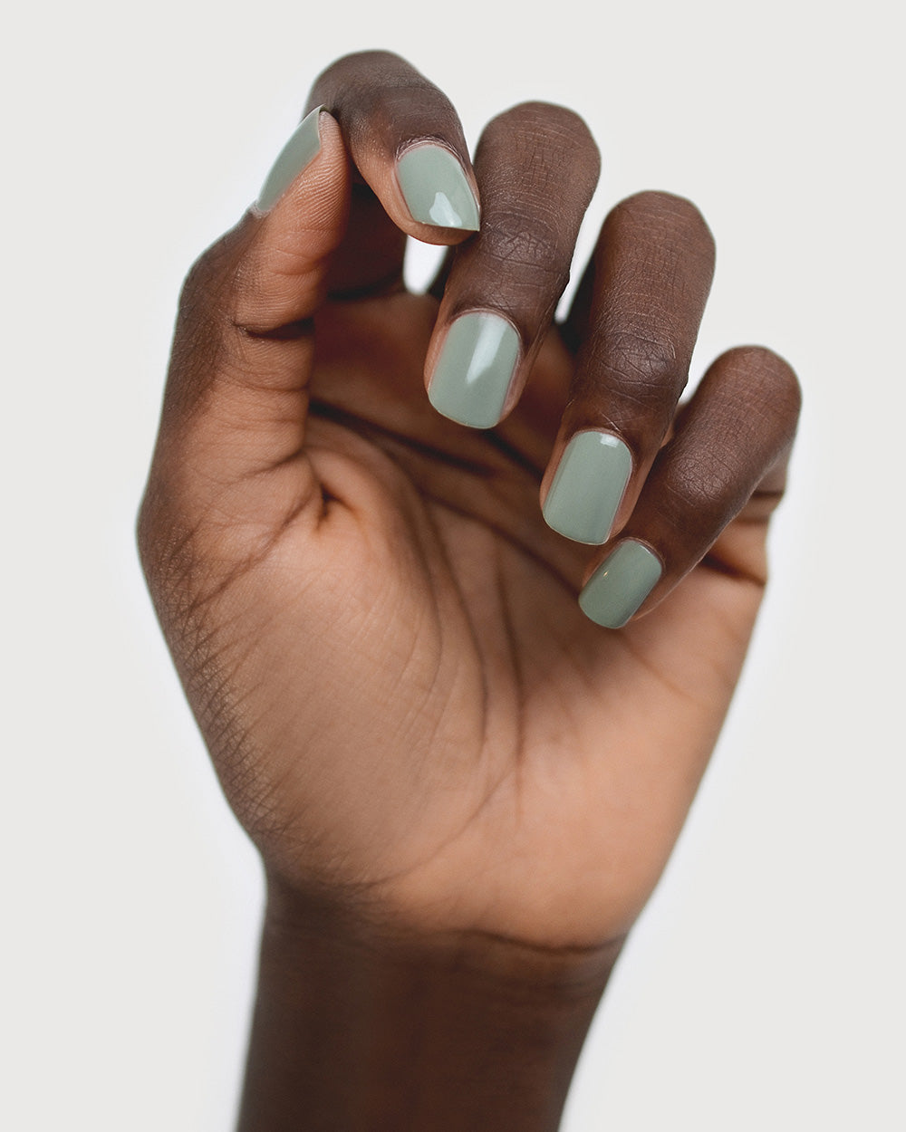 Dark skin hand wearing Soundscape sage green crème nail polish by Sienna Byron Bay