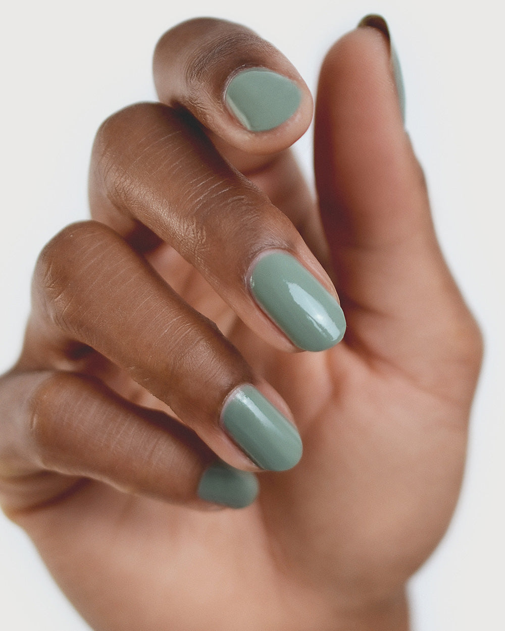 Medium tanned skin hand wearing Soundscape sage green crème nail polish by Sienna Byron Bay close-up