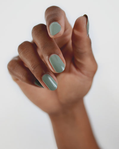 Medium tanned skin hand wearing Soundscape sage green crème nail polish by Sienna Byron Bay