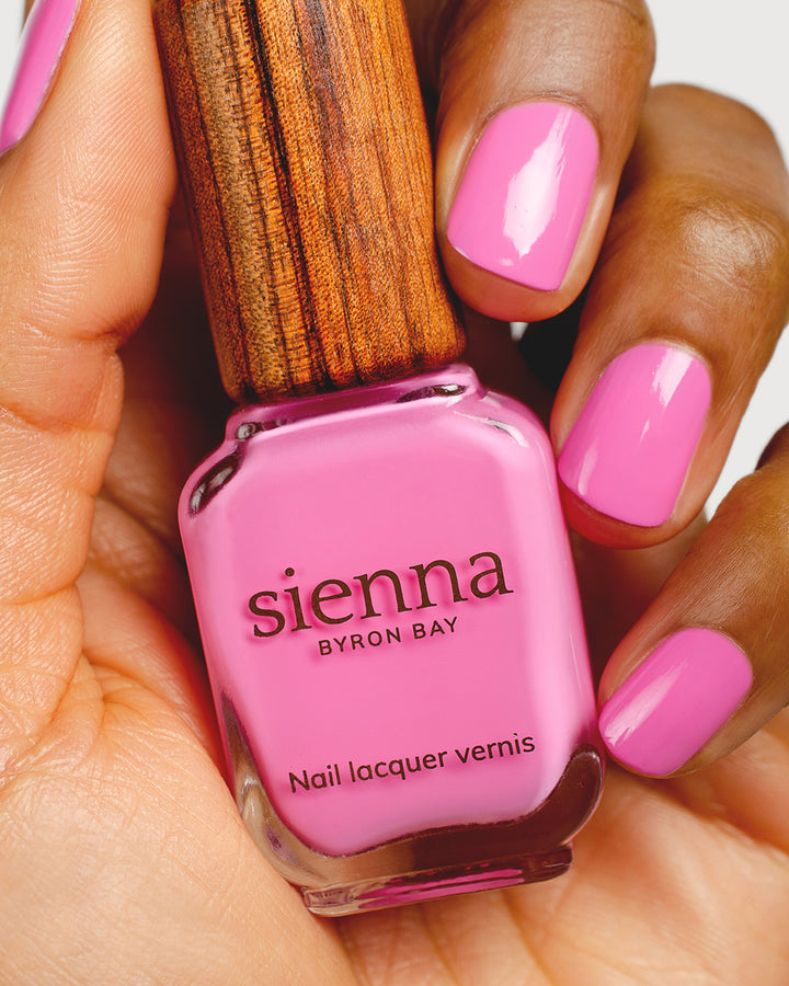Bright mid-tone fuchsia nail polish hand swatch on medium skin tone holding sienna bottle close-up