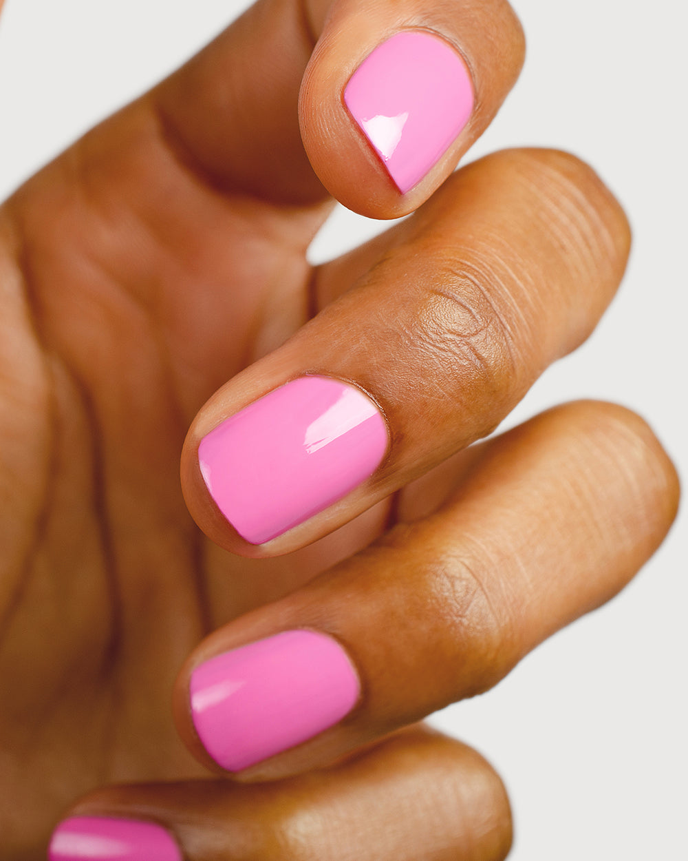 Bright mid-tone fuchsia nail polish hand swatch on medium skin tone up close