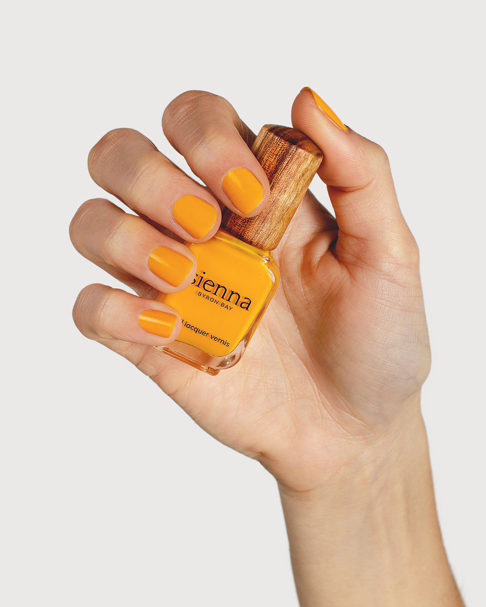 Sunflower yellow nail polish hand swatch on fair skin tone holding sienna bottle
