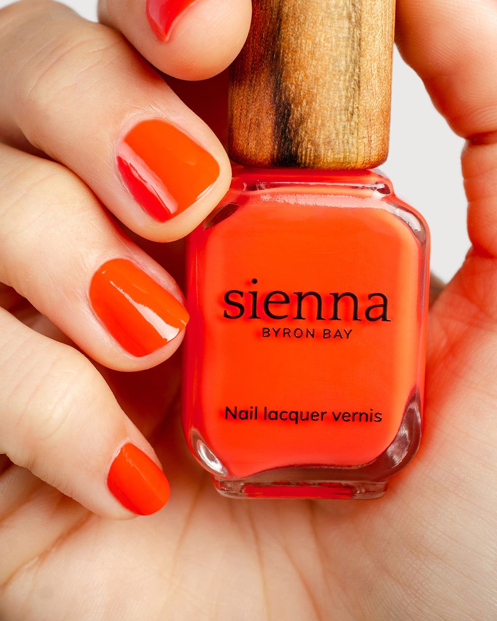 Tangerine nail polish hand swatch on fair skin tone holding sienna bottle close-up