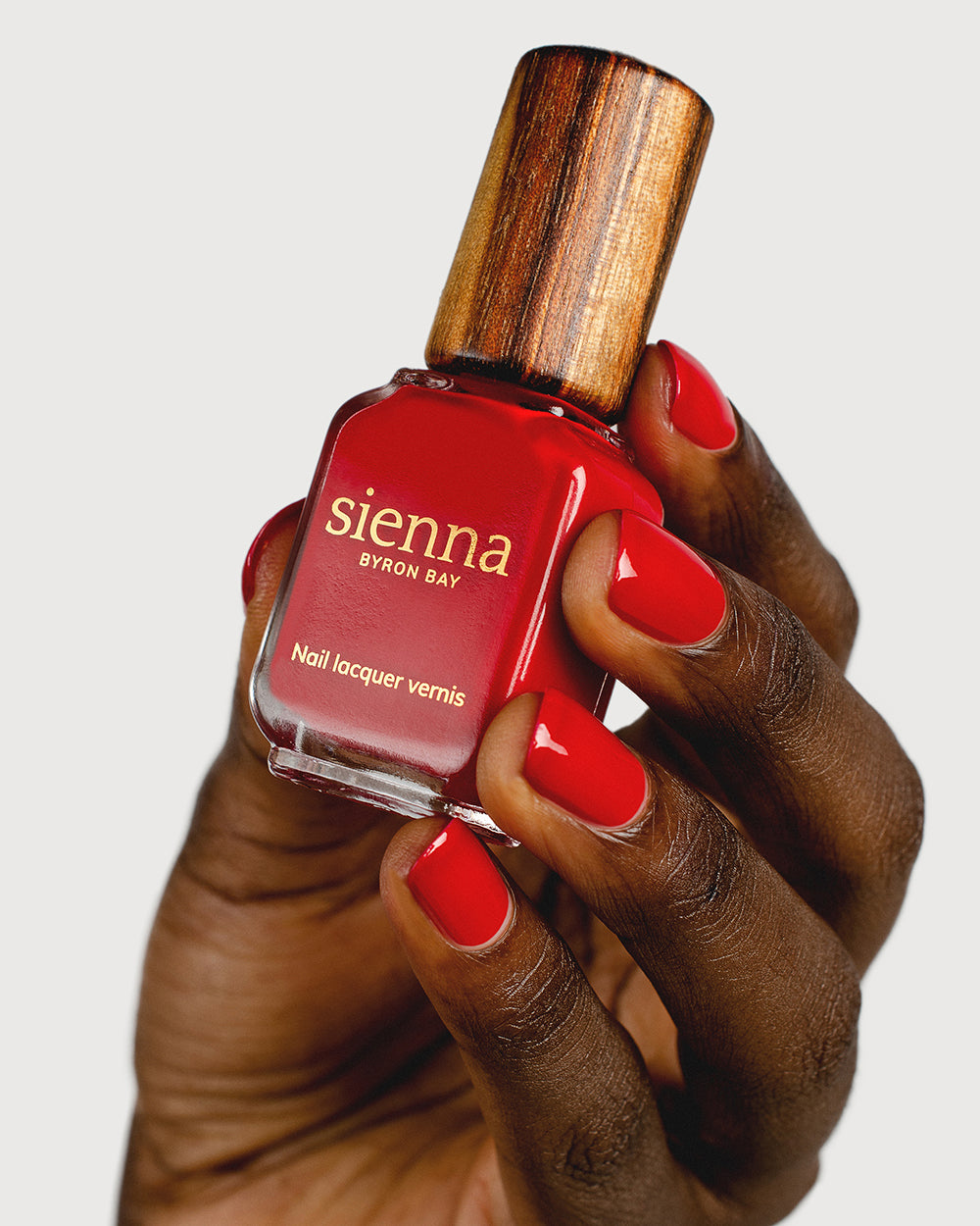 Classic red nail polish hand swatch on dark skin tone holding sienna bottle