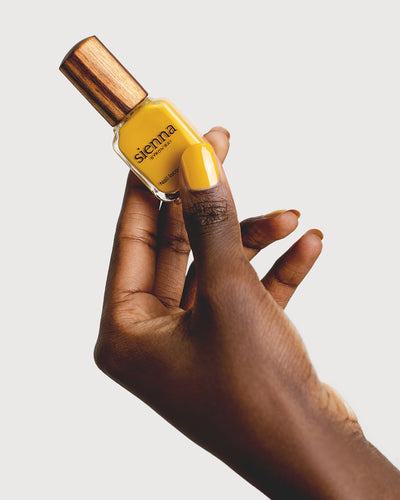 Tuscan sun yellow nail polish hand swatch on dark skin tone holding sienna bottle