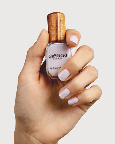 Light lilac pastel nail polish hand swatch on fair skin tone holding sienna bottle