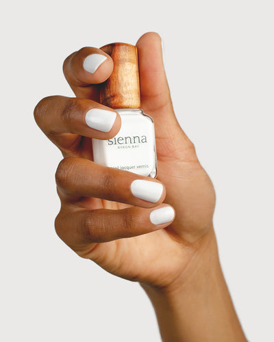 Crisp snow white nail polish hand swatch on medium skin tone holding sienna bottle